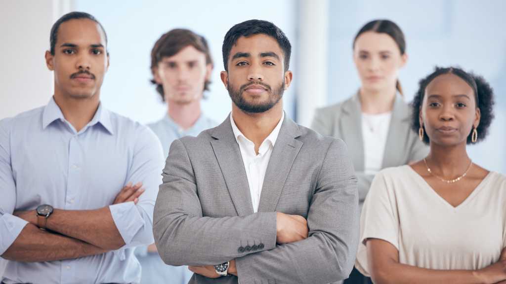group of five business professionals standing with arms crossed looking confident or defiant